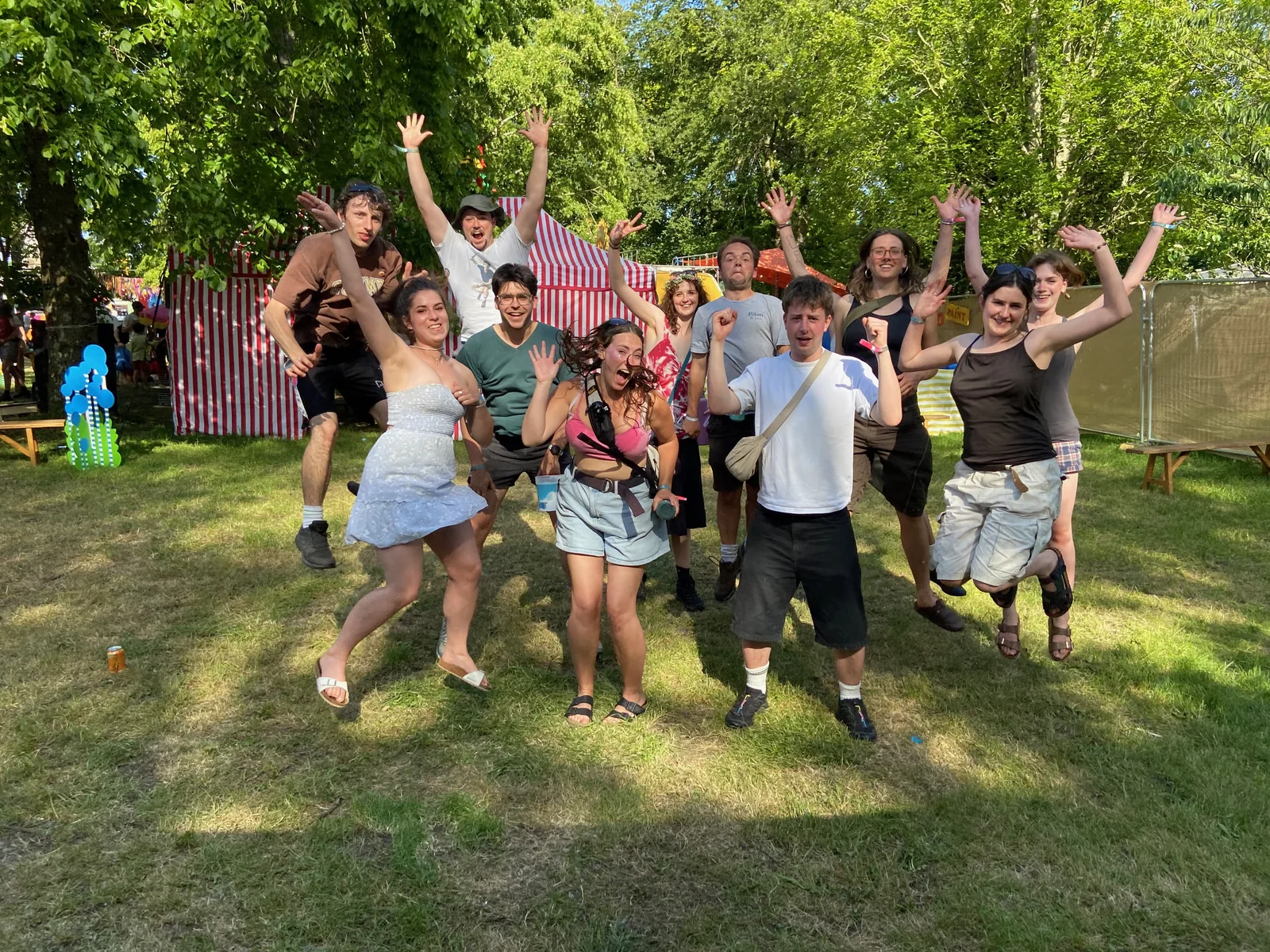 About a dozen young volunteers leap into the air with their arms raised on the grass at a Gloucestershire park, a red-and-white striped circus tent behind them, promoting The Great Big Climate Circus.