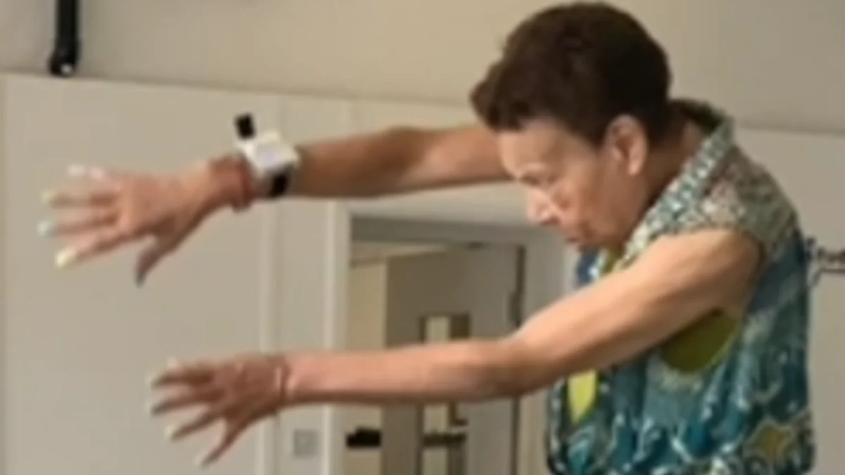 A woman taking part in a Parkinson's Steppers session in Leeds, arms outstretched mid-movement, wearing the programme's sound-making technology on her wrist.