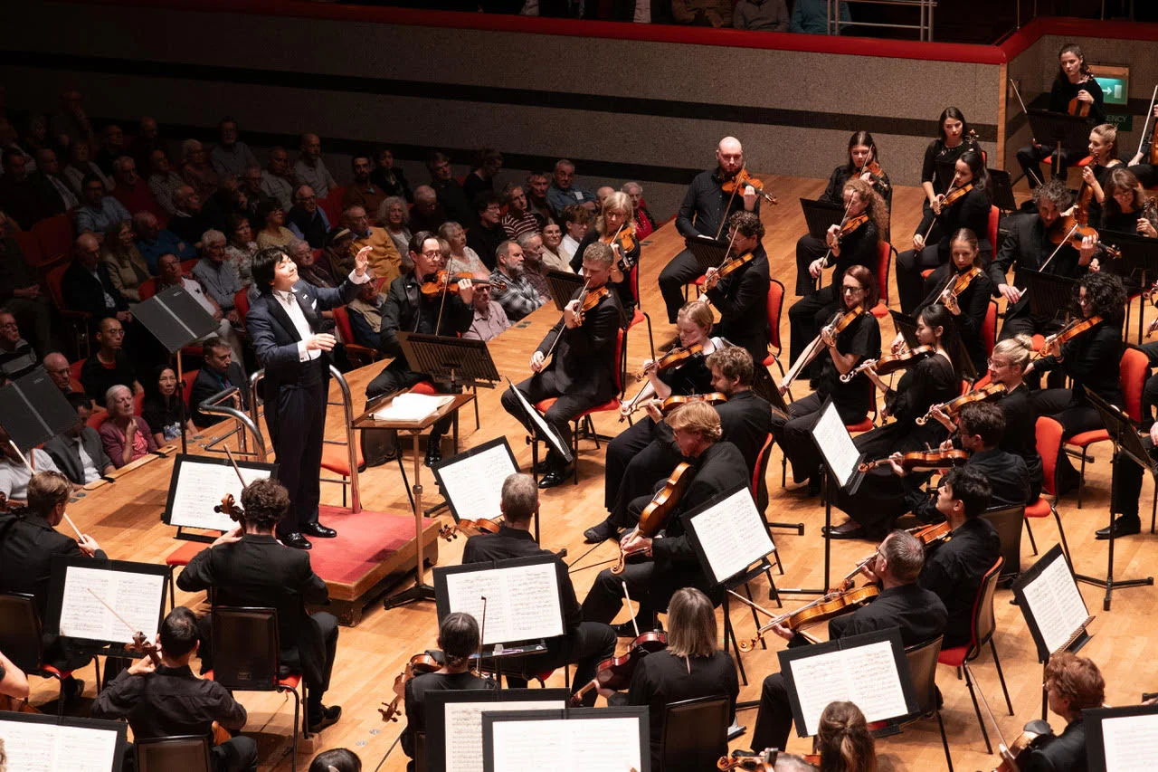 Kazuki Yamada conducts the CBSO with string players around his podium and the audience seated behind.