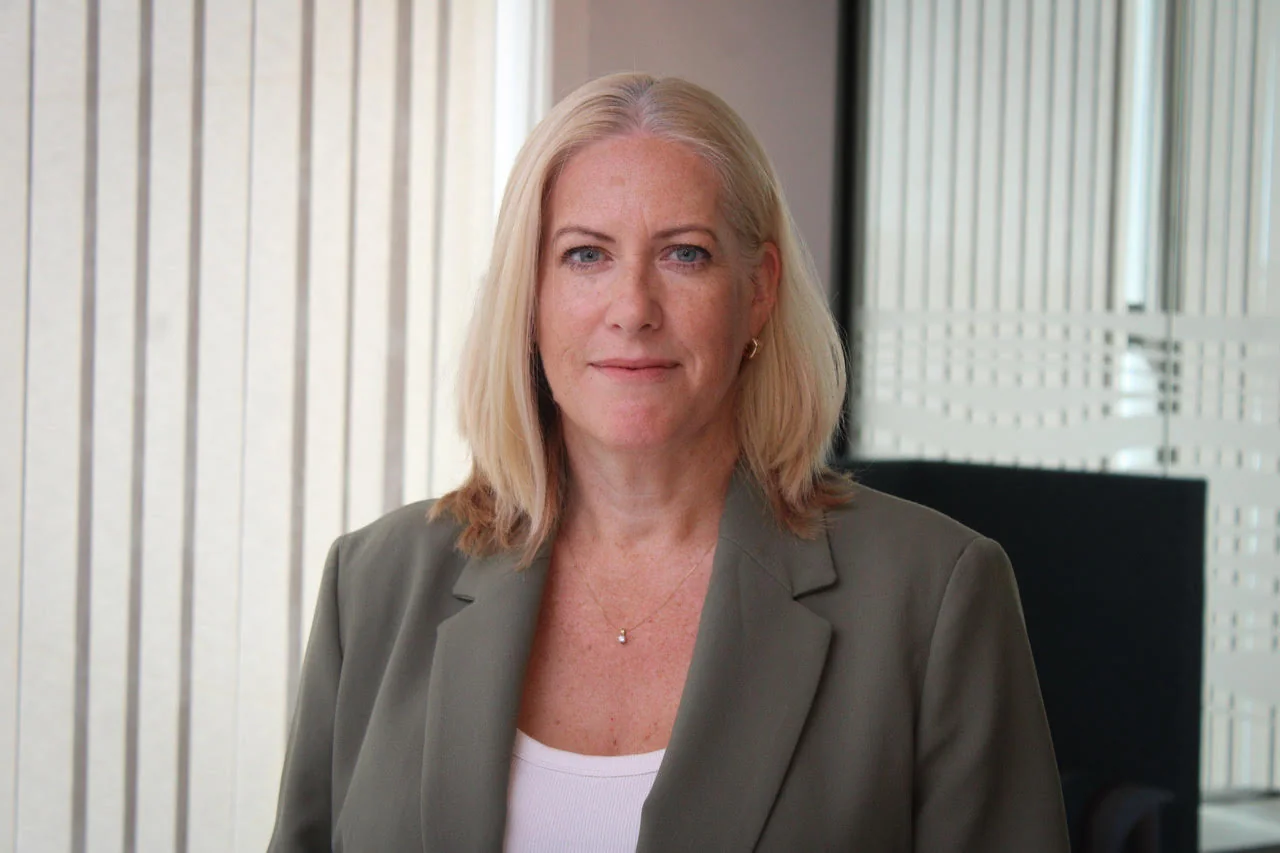 Jo Morris, Head of Insight at Novuna Business Finance, wearing a sage green jacket and standing in a bright office with vertical blinds behind her.