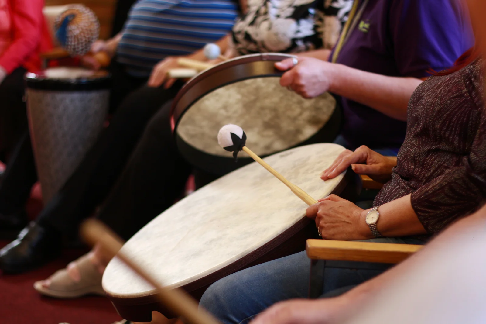 Participants seated in a circle holding hand drums and soft mallets during a community drumming and percussion session.