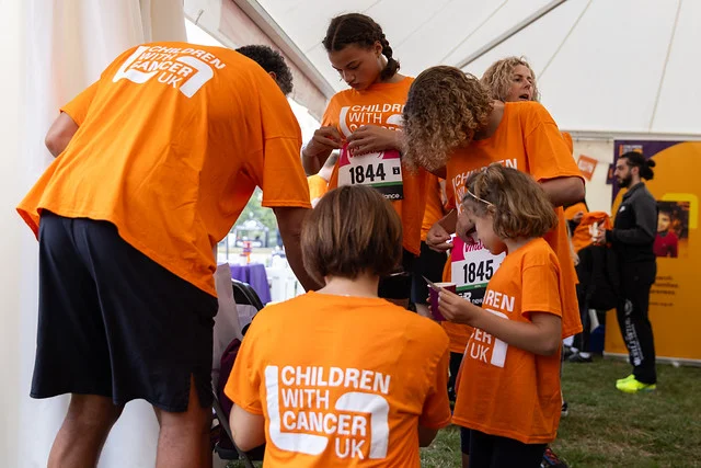 Children and adults in orange Children with Cancer UK shirts prepare race numbers inside the charity tent at a previous Westminster Mile.